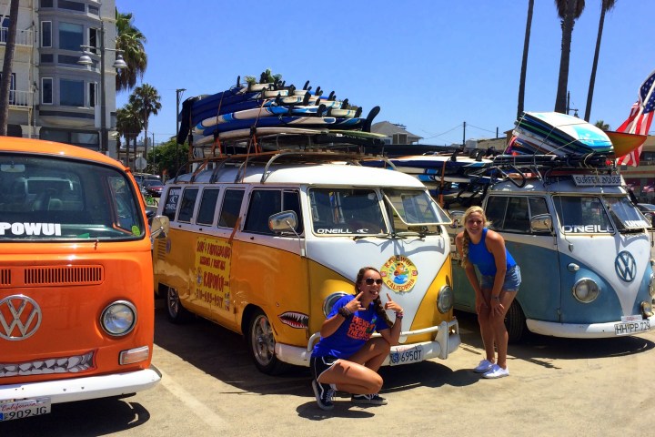 2 girls stnading in front of vans on the beach.