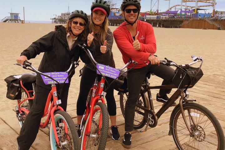 3 people sitting on a bike at the beach.